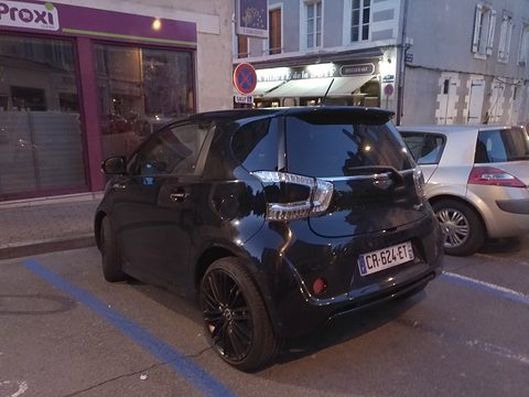 Black city car from the rear quarter in a town street at dusk, shopfronts behind. Opens a larger view