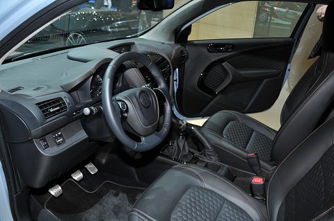 Black quilted leather seat, steering wheel and dashboard with orange stitching, seen through the open door.