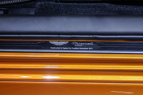 Black sill plate with the Aston Martin wings and Cygnet script above orange paint. Opens a larger view