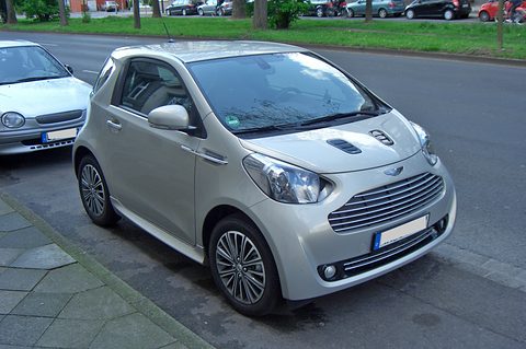 Silver city car with a chrome slatted grille parked beside a grass verge. Opens a larger view