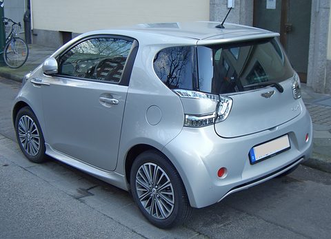Silver city car from behind, showing its rear lamps and roof spoiler, parked at a kerb. Opens a larger view