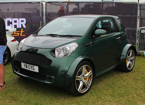 Dark green city car with wide wheel-arch extensions and large alloy wheels on grass.
