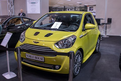 Yellow city car behind a rope on a show stand, a Noble House sign on its bumper. Opens a larger view