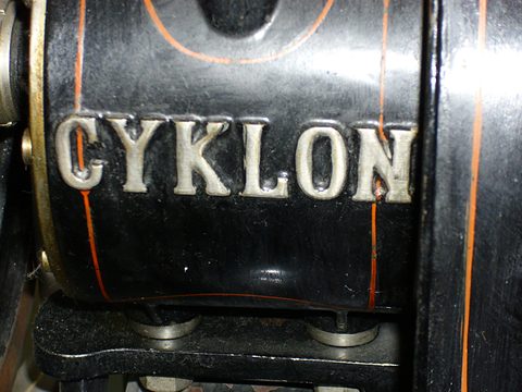 Close view of silver raised letters reading CYKLON on a black casing with orange lines. Opens a larger view