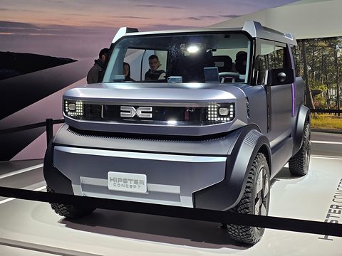 Grey boxy small concept with a light-bar grille and HIPSTER plate behind a rope, a forest mural behind. Opens a larger view