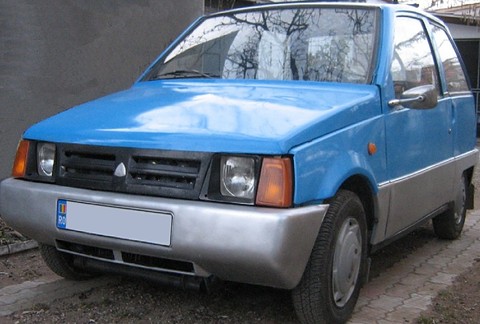 Small blue three-door hatchback with grey plastic bumpers and orange indicators, parked on a brick drive.