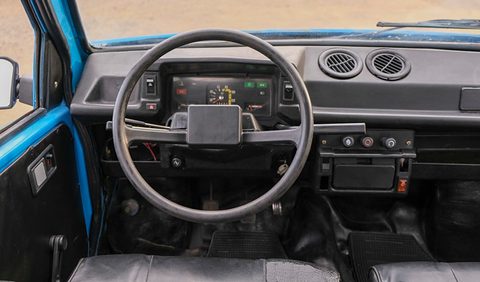 Two-spoke steering wheel before a black plastic dashboard with a small instrument binnacle and two round air vents.