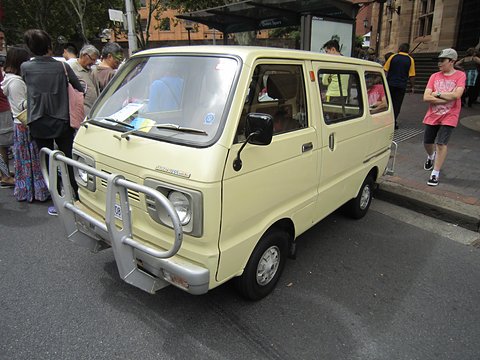 Cream small cab-over van with a chrome bull bar parked on a street, people walking past. Opens a larger view