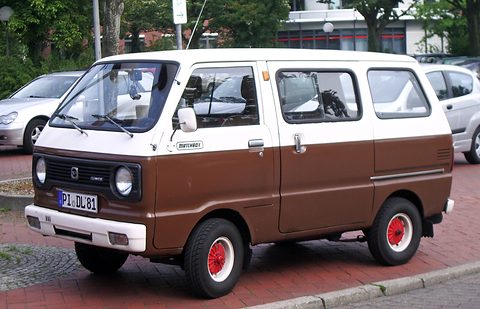 Brown and white small cab-over minibus with red wheels parked on red brick paving. Opens a larger view