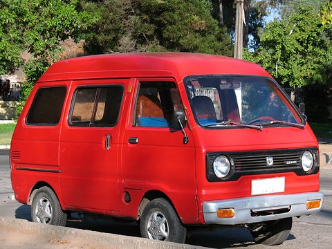 Red small high-roof van parked on a sunny street under trees. Opens a larger view
