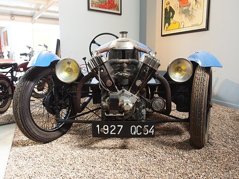 Low front view of a V-twin engine between two yellow-lensed headlamps, a number plate below. Opens a larger view