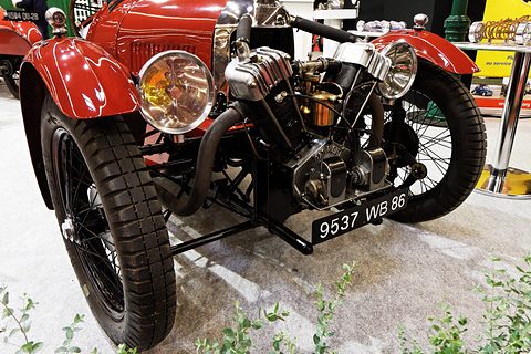 Front view of a red three-wheeler: polished V-twin, two headlamps and a number plate. Opens a larger view