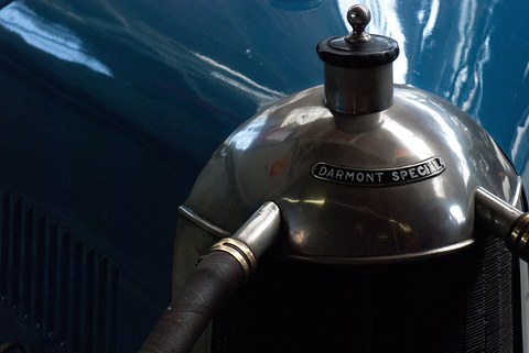 Close view of a polished radiator cowl with a filler cap and an enamel badge reading Darmont Spécial, blue bodywork behind. Opens a larger view