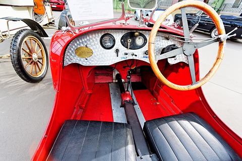 An engine-turned aluminium dashboard with round dials, a wooden-rimmed wheel and black seats in a red body. Opens a larger view