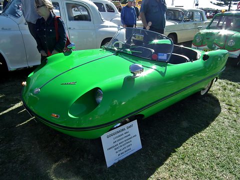 Bright green open roadster on grass with a display card in front, visitors behind.