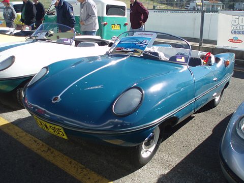 Blue open roadster parked in a row of Darts, with a 50 Years Goggomobil sign on its windscreen. Opens a larger view