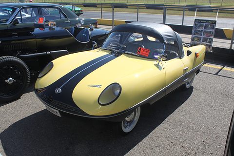 Yellow roadster with a black centre stripe and a black hardtop, parked on tarmac.