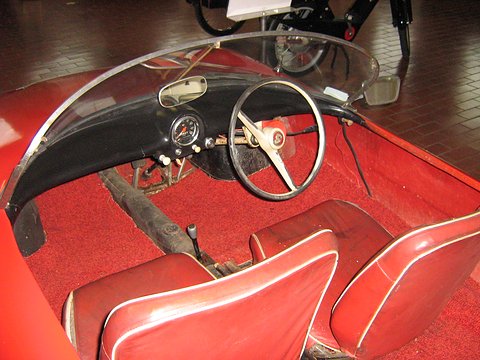 Looking into an open red car: a thin steering wheel, a small instrument panel and red bucket seats. Opens a larger view