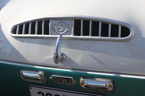 Close view of a white tail with a slotted chrome grille and handle above a teal panel with a BUCKLE plate. Opens a larger view