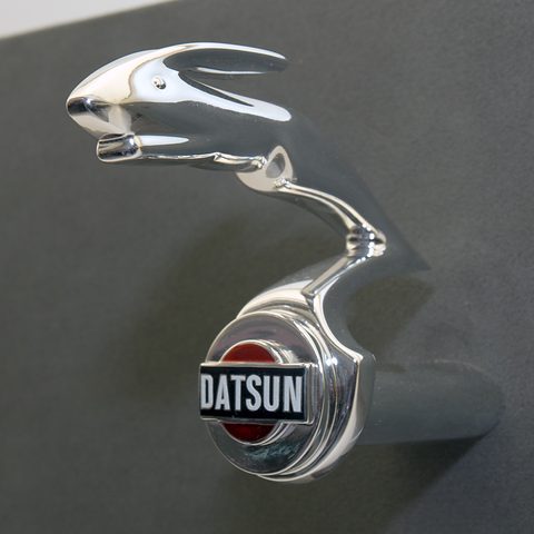 A chrome mascot of a stretched leaping hare on a radiator cap above a round red Datsun badge.