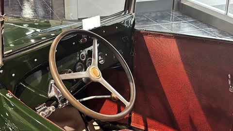 A thin cream steering wheel in front of a small dark green dashboard, a red leather seat to the right. Opens a larger view