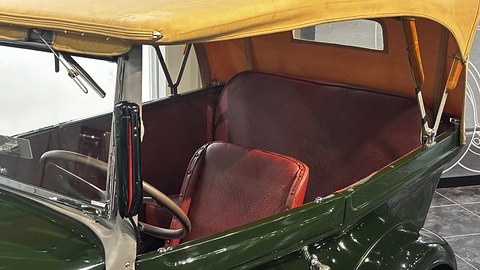 Looking into an open car under a tan hood: red buttoned leather front and rear seats and a steering wheel. Opens a larger view