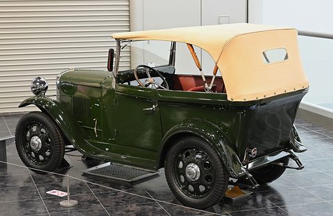 The rear quarter of a dark green open tourer with a cream hood, rear spare wheel and black wings. Opens a larger view