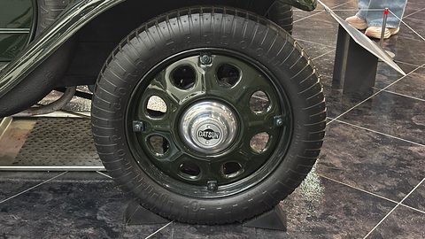 A black tyre on a dark green steel wheel with round holes around a chrome hub cap. Opens a larger view