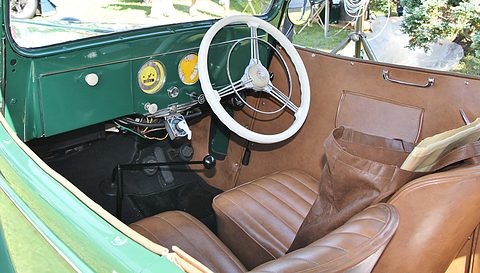 The cockpit of a green open tourer: a cream steering wheel, round dials and brown leather seats. Opens a larger view