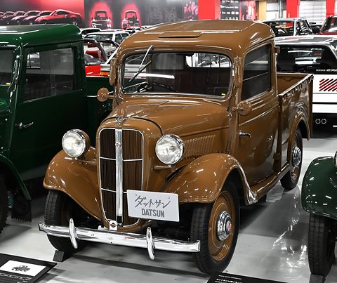 A small brown pick-up truck with a chrome grille and black wings in a garage hall. Opens a larger view