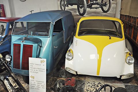 A pale blue three-wheeled van and a white and yellow bubble car side by side, an information board propped in front. Opens a larger view