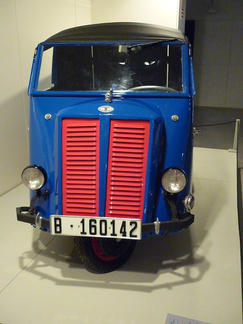 Head-on view of a small blue van with a split red louvred grille, two headlamps and a black roof. Opens a larger view
