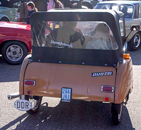 Rear of a tan three-wheeler with a black hood, a DUO 4/1 badge, a small blue plate and a DDR oval sticker. Opens a larger view
