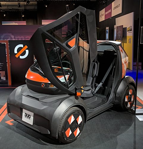 Grey and black tiny two-seater with a big upward-opening door, showing a seat inside.