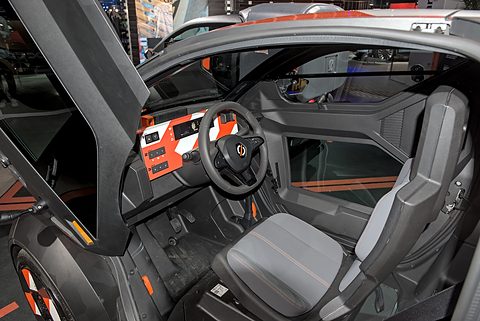 Grey driver’s seat, a small steering wheel and an orange dashboard panel seen through the open door.