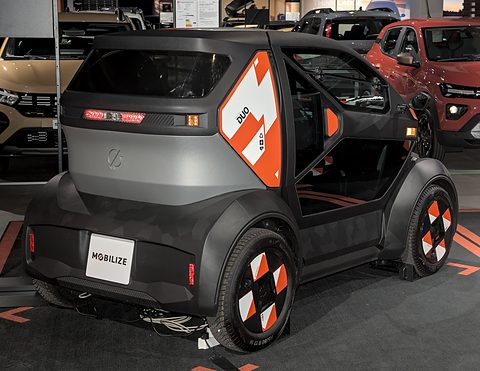 Rear of a grey and black tiny two-seater with orange graphics and chequered wheel covers. Opens a larger view