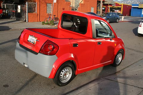 Rear of a red small pickup with a grey bumper, open bed and California plate on a street. Opens a larger view