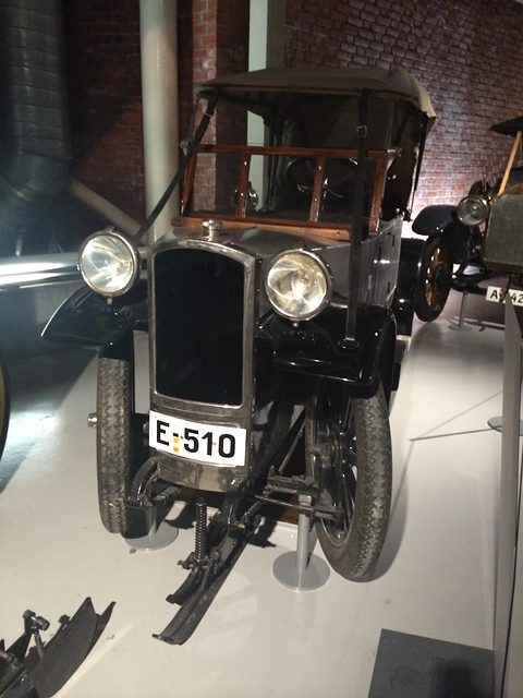 Front view of a narrow grey car with two headlamps, a folding top and wheels with skis fitted below, plate E 510. Opens a larger view