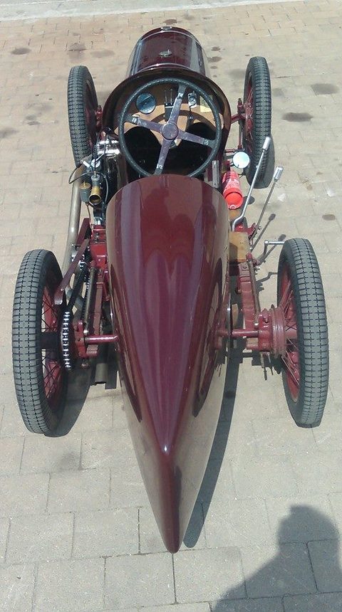 Overhead view of a slender maroon single-seater with a four-spoke steering wheel, chain drive and spoked wheels. Opens a larger view