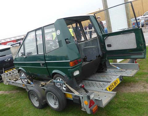 Green car on a trailer with its rear door open onto an empty floor space inside. Opens a larger view
