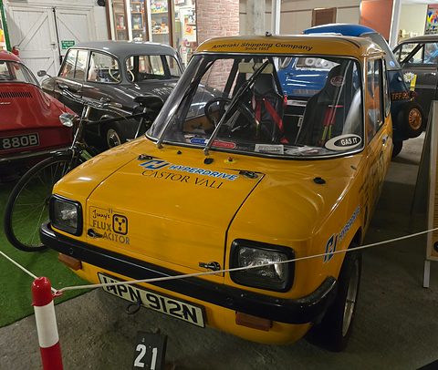 Yellow electric car with decals including a Flux Acitor joke sticker, parked behind a rope. Opens a larger view
