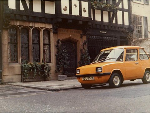 Orange electric car parked before a black-and-white timbered house. Opens a larger view