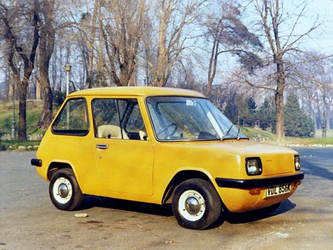 Yellow electric car parked on a path among bare trees. Opens a larger view