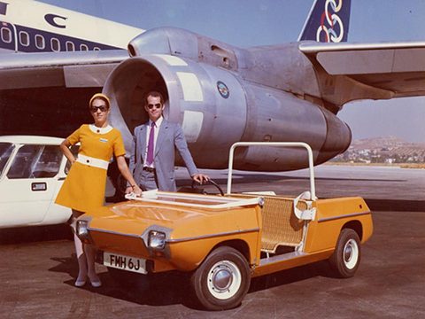 Orange open car with a wicker seat, a uniformed woman and man posing by a jet engine. Opens a larger view
