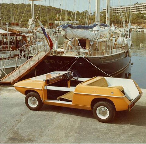 Orange doorless car with white seats parked on a quay beside a moored yacht. Opens a larger view