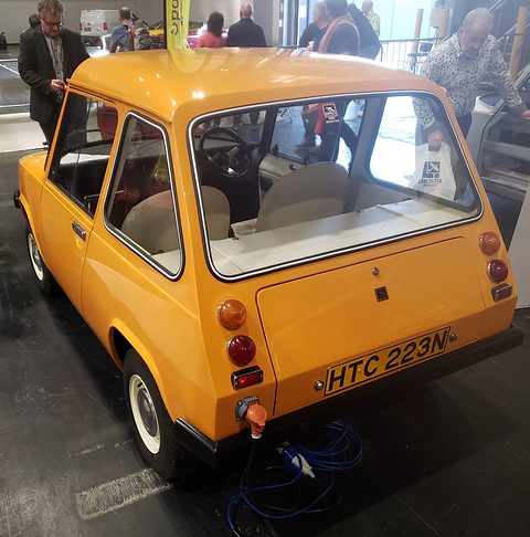 Yellow electric car from the rear quarter, a blue charging cable trailing from its tail.