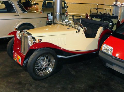 Cream and red open roadster with an upright chrome radiator, wire wheels and cycle wings among other cars.