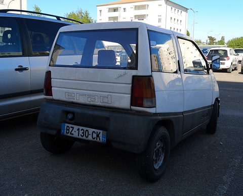 Back of a small white hatchback with tall rear lamps and a plate BZ-130-CK, parked among larger cars in sunshine. Opens a larger view