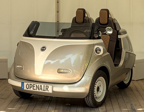 Silver open bubble car without a roof, with brown quilted seats and an OPENAIR plate, on a wooden floor. Opens a larger view