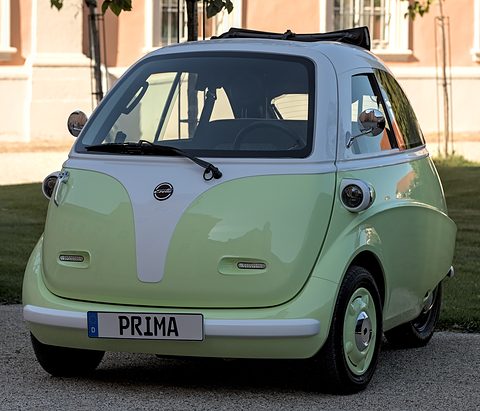 Pale-green and white bubble car with a PRIMA plate on gravel in front of a palace building.